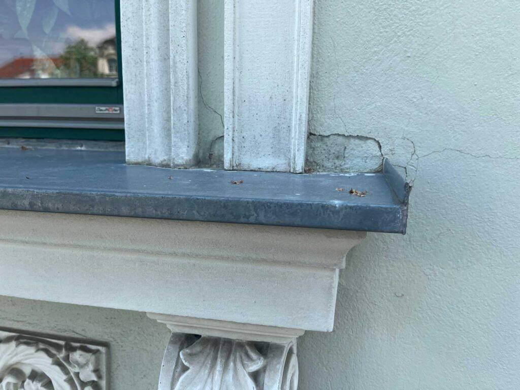 Detailaufnahme einer Übergangsstelle zwischen Fassadenverblechung und Putzfassade mit Rissbildung.