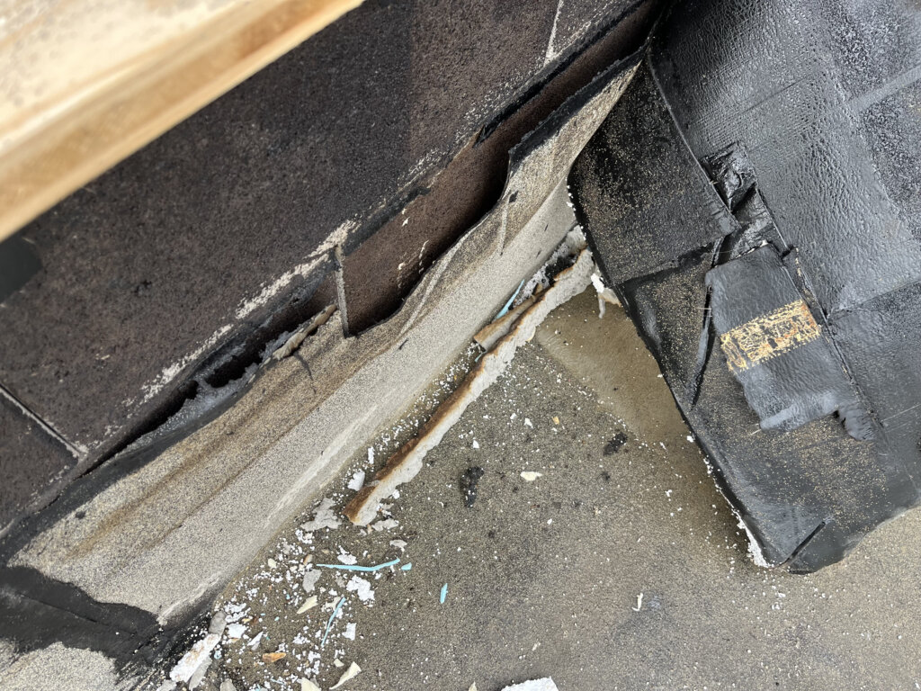 Beschädigte schwarze Dachrinne mit Rissen und abgebröckeltem Material an einer Gebäudeecke