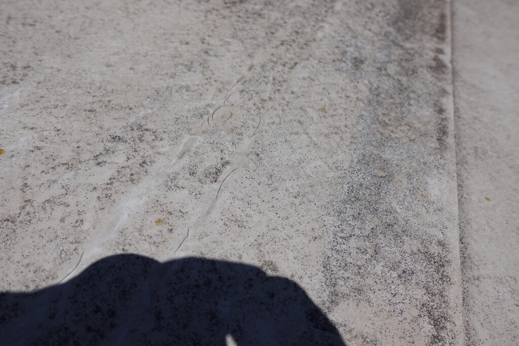 Betonboden mit Rissen und Schatten einer Person, die darauf steht