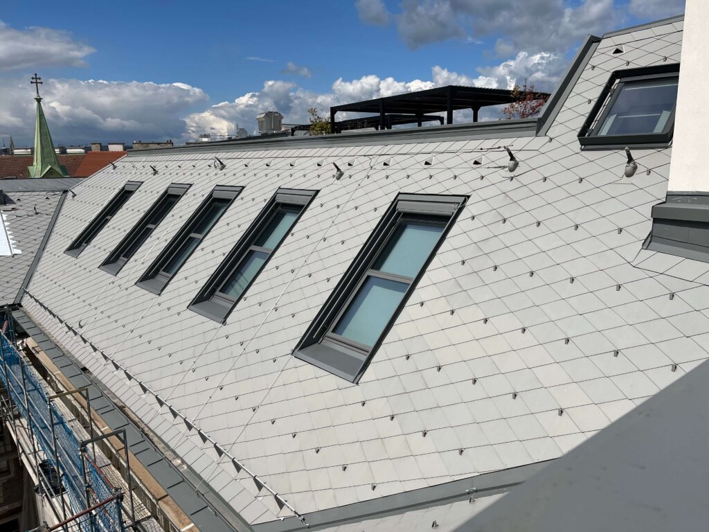 Dachfenster in modernem Schieferdach mit Dachterrasse unter blauem Himmel