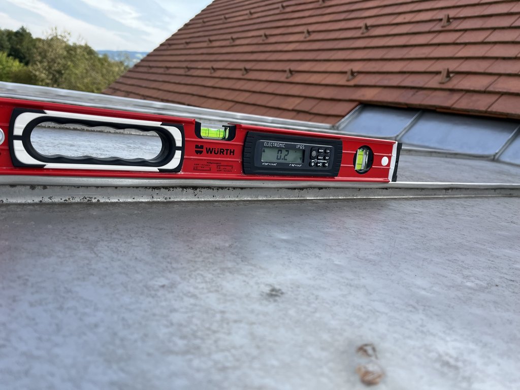 Würth elektronische Wasserwaage zeigt 0,2 Grad auf Flachdach mit rotem Ziegeldach im Hintergrund