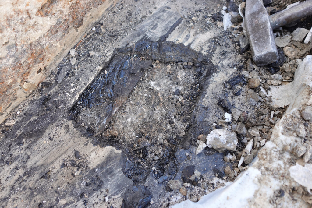 Dunkle Asphaltmasse mit Steinbrocken und Bauschutt auf einer Baustelle