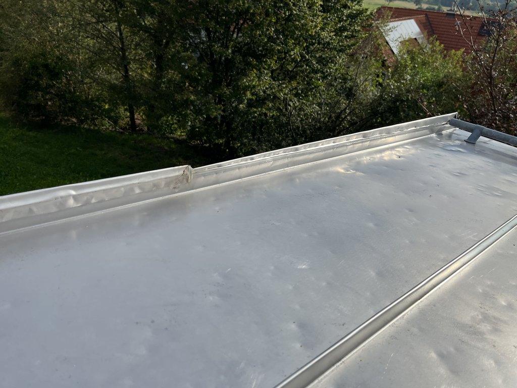 Flachdach mit grauer PVC-Abdichtung und Metalleinfassung vor grüner Landschaft