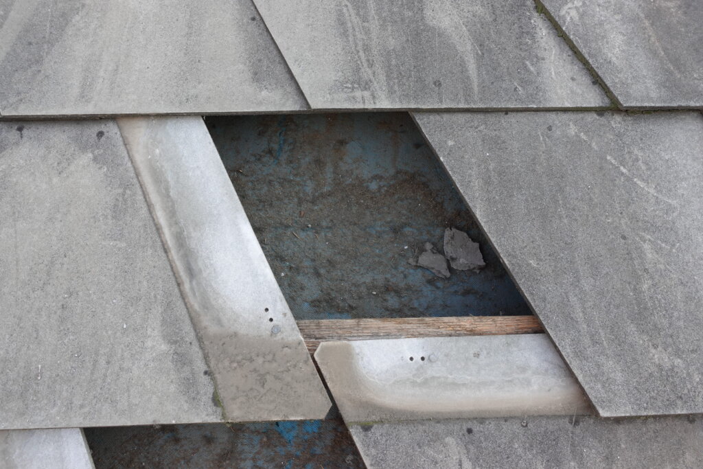 Beschädigte Dachziegel mit fehlenden Teilen und sichtbarer Unterdeckung aus Holz und Metall