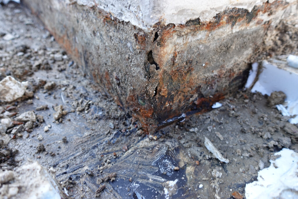 Rostiges Metall mit Korrosion und abblätternder Farbe an einer feuchten Betonoberfläche