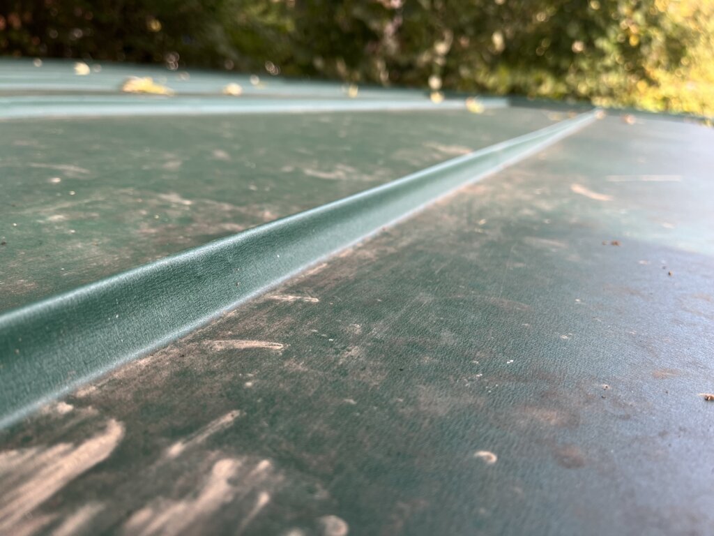 Grünes Metalldach mit abgeblätterter Farbe und sichtbaren Verschleißspuren im Sonnenlicht