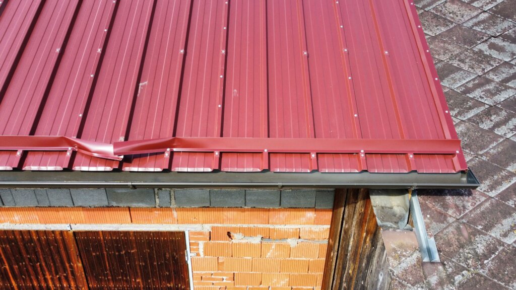 Rotes Wellblechdach mit Schneefang auf Ziegelmauerwerk aus der Vogelperspektive