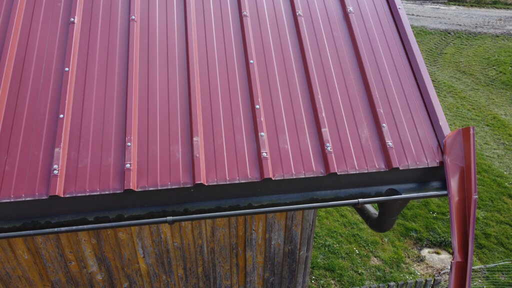 Rotes Wellblechdach mit schwarzer Regenrinne an landwirtschaftlichem Gebäude