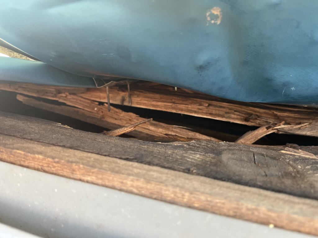 Beschädigte Holzpalette unter blauem Metallcontainer mit sichtbaren Rissen und Brüchen